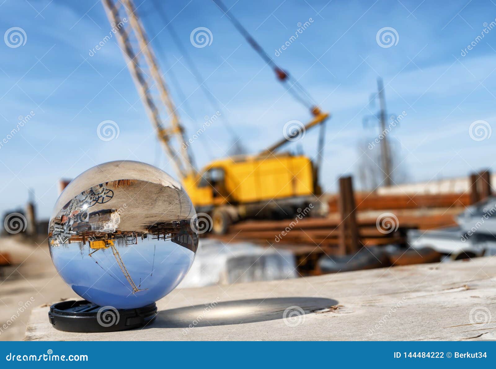 View of base of building materials with a large crane through an optical lens ball. View of the base of building materials with a large yellow crane through an optical glass ball