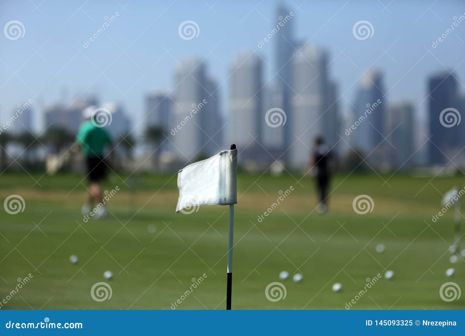 a flag on golf course amid golfers, balls and skyscrapers in dubai