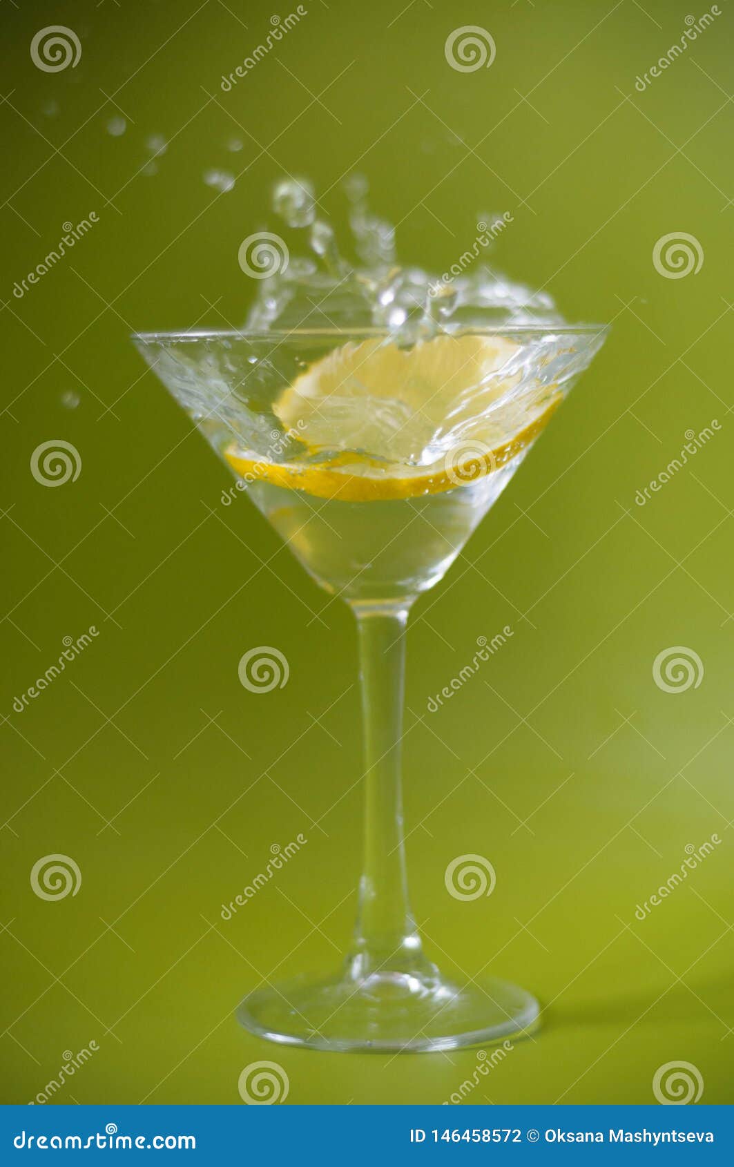 A limoncellos slice falling in a fresh cocktail, water drops on a green background