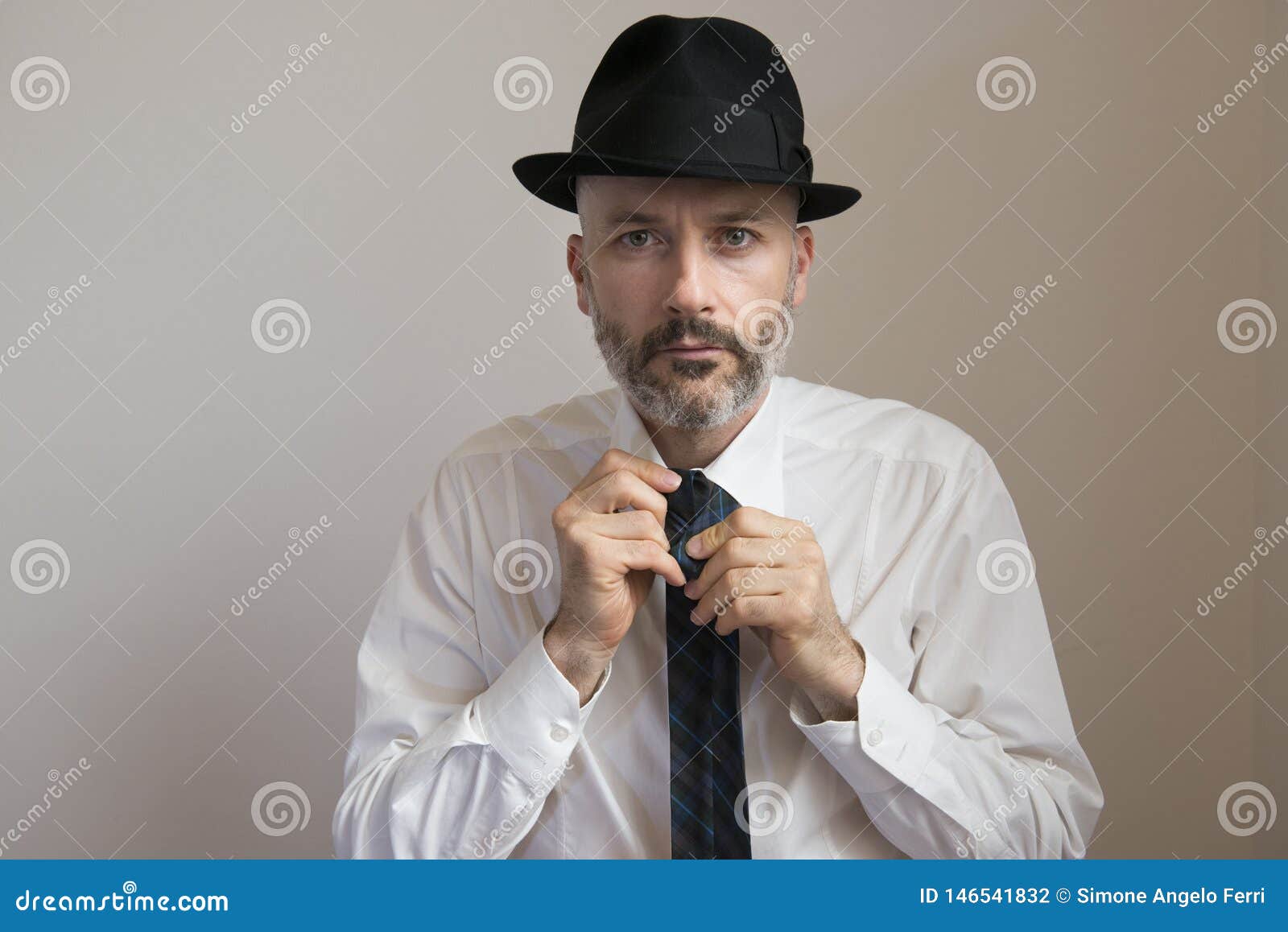 Adult man with hat and beard is knotting his necktie. Caucasian white man portrait with hat and beard is knotting his necktie in white background.