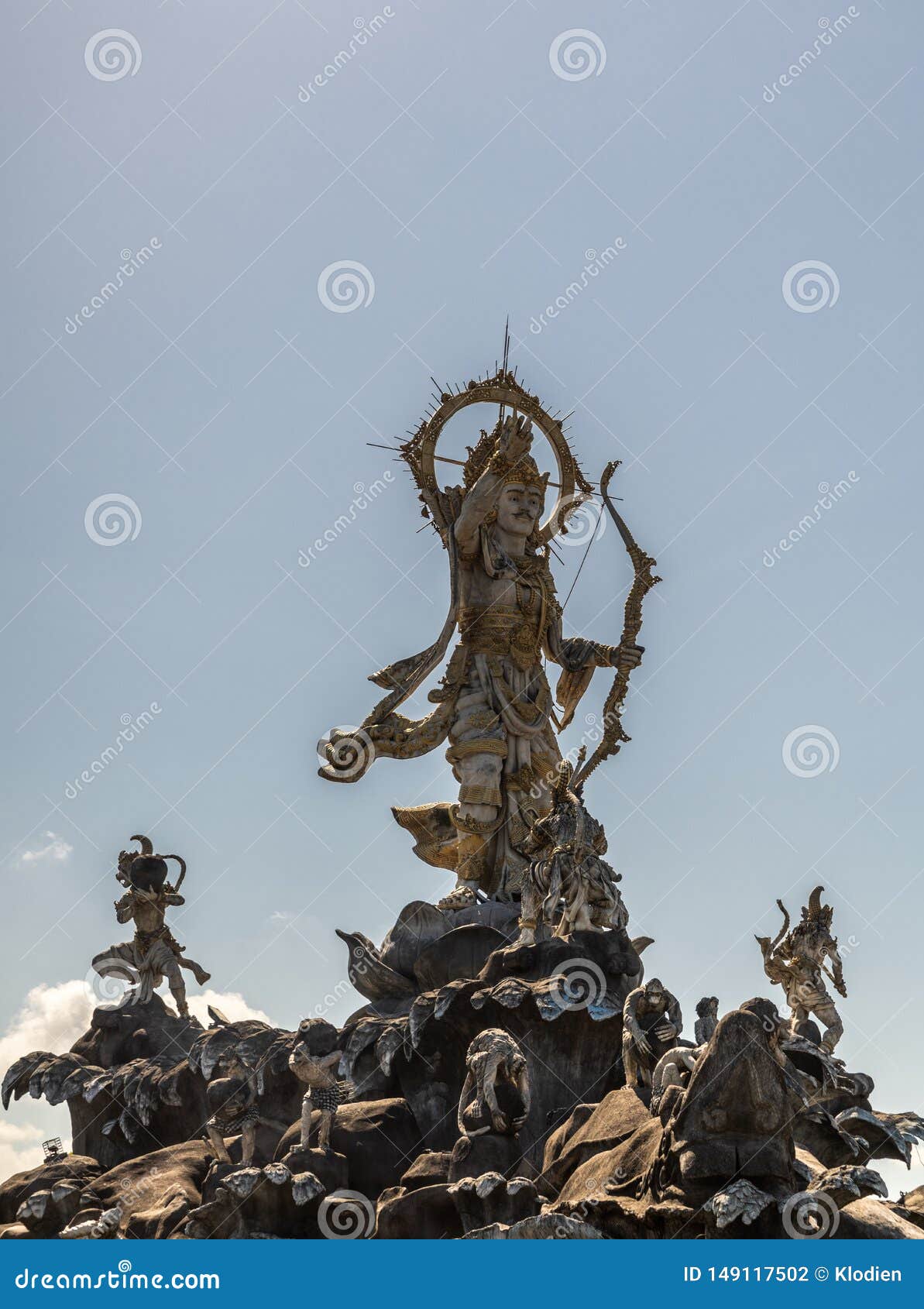 Patung Titi Banda statue in Denpasar, Bali Indonesia. Denpasar, Bali, Indonesia - February 26, 2019: Closeup of Patung Titi Banda brown stone statue of holy warrior in center of roundabout of By Pass Ngurah Rai Street under light blue sky