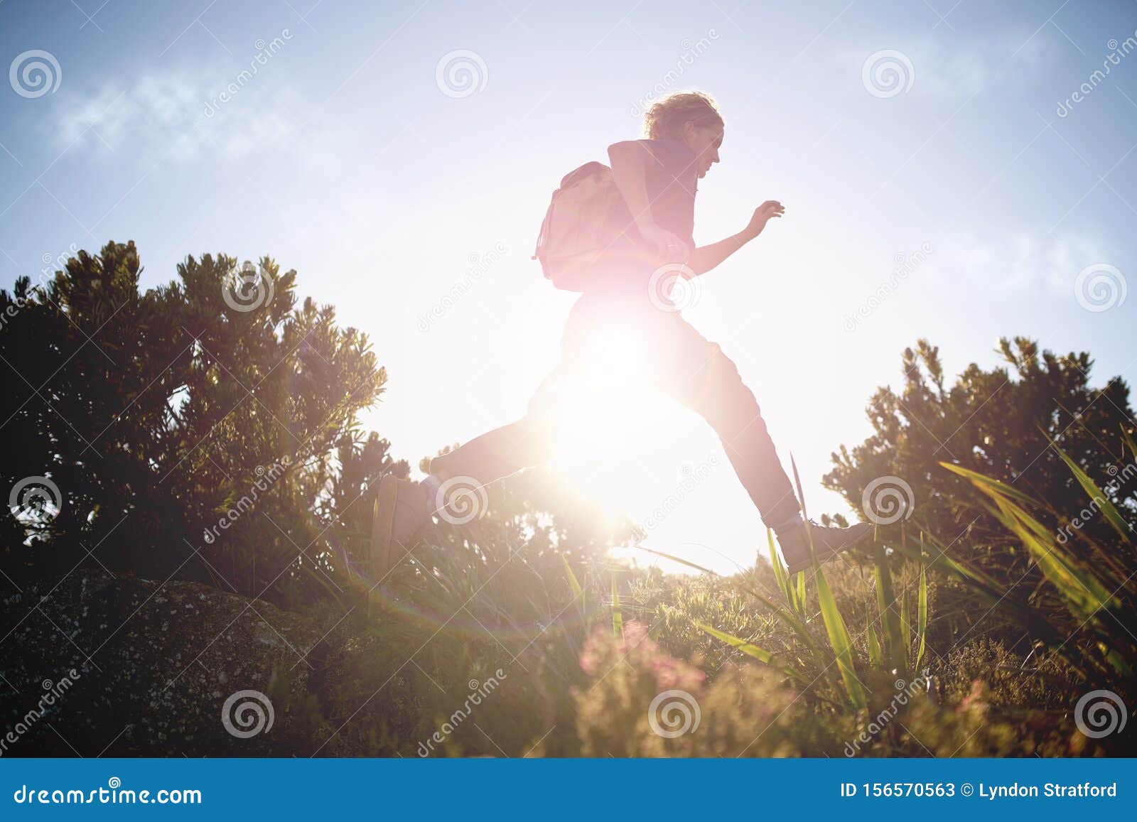 Male hiker running while hiking on sunny day. Low angle view of male tourist with his backpack running while hiking in the countryside on sunny day