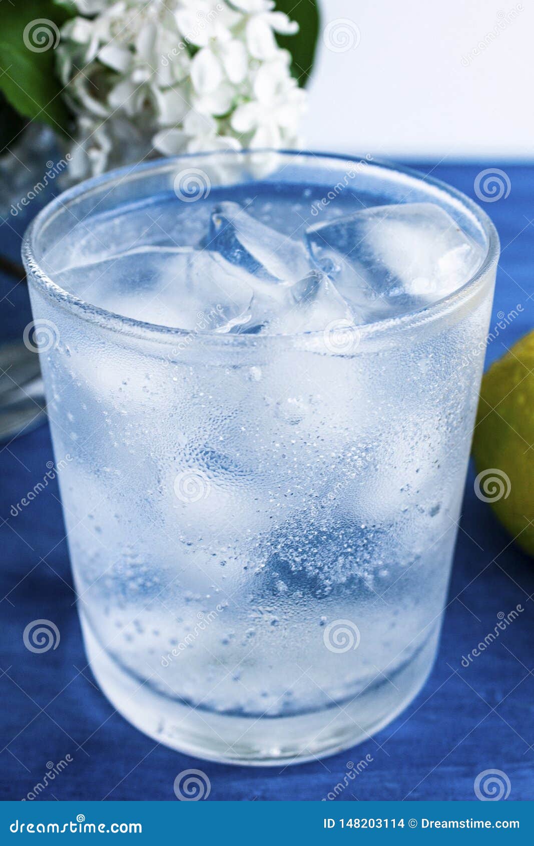 A Glass of Cold Water with Ice and Lemon on a Blue Background