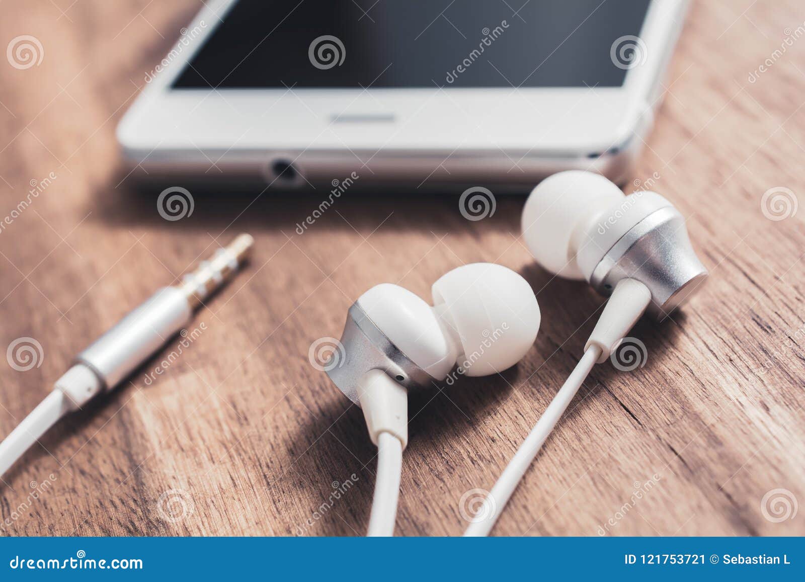 InEar Headset and it`s Cable Lying in Front of a White Smartphone`s Headphone Jack Stock Image