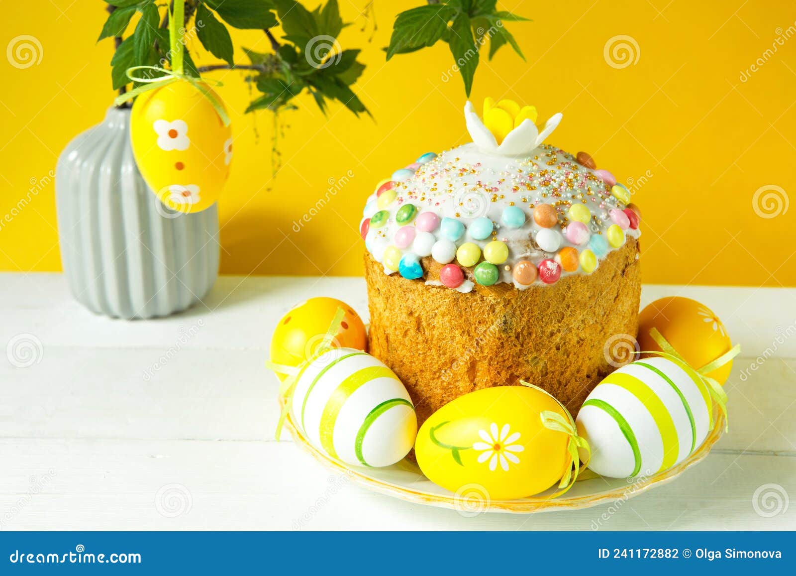 easter cake with painted eggs on a platter in a white table. traditional festive food. yellow background