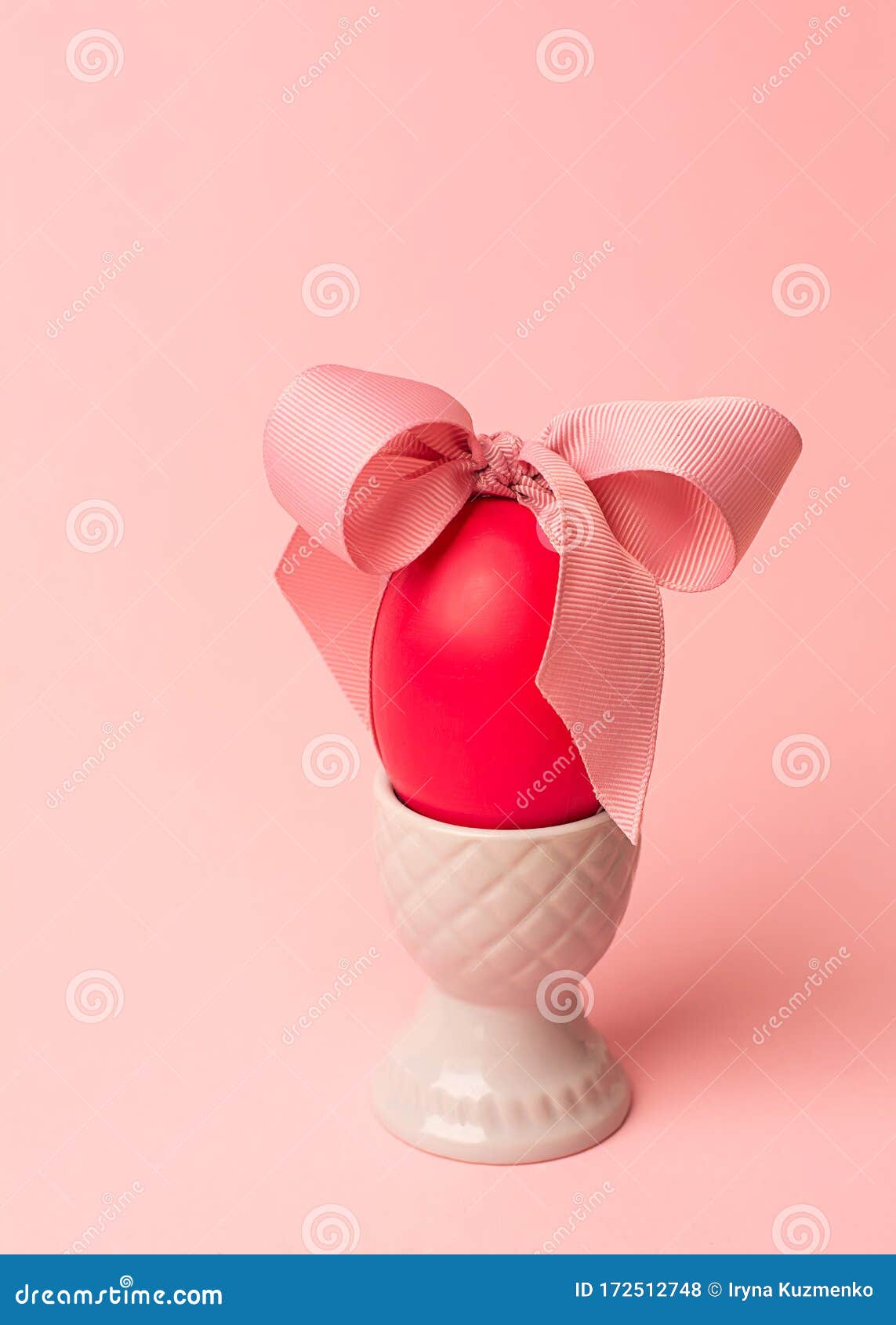 easter creative concept. one red egg tied with a pink ribbon standinng in the gray egg cup a on a pink background. minimalism,