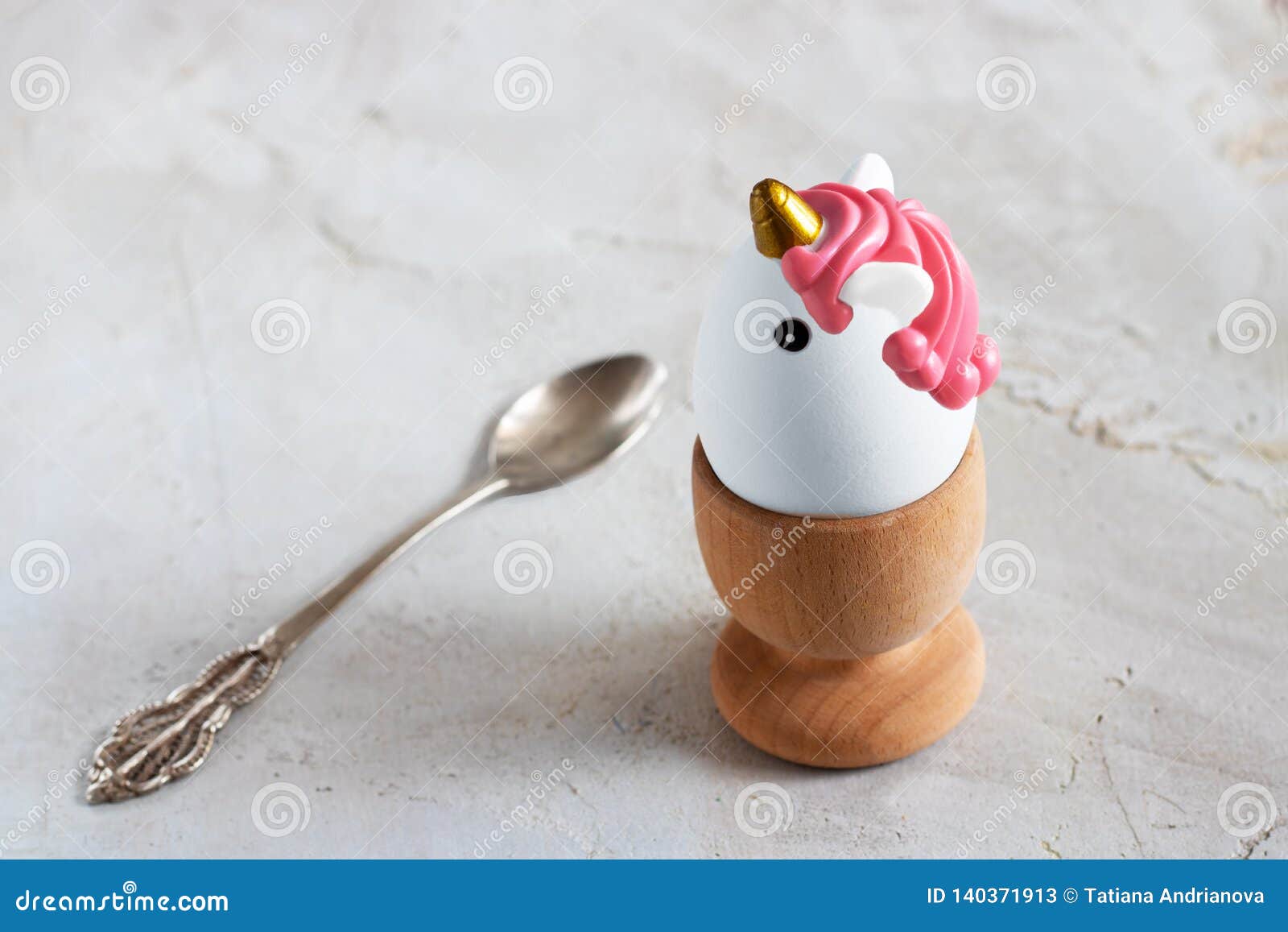 white egg in wooden egg cup and tea spoon on grey cement textured background, horizontal banner, copy space, breakfast, easter,