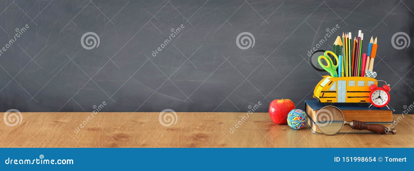 education and back to school concept. pencils stand as bus over wooden desk infront of classroom blackboard