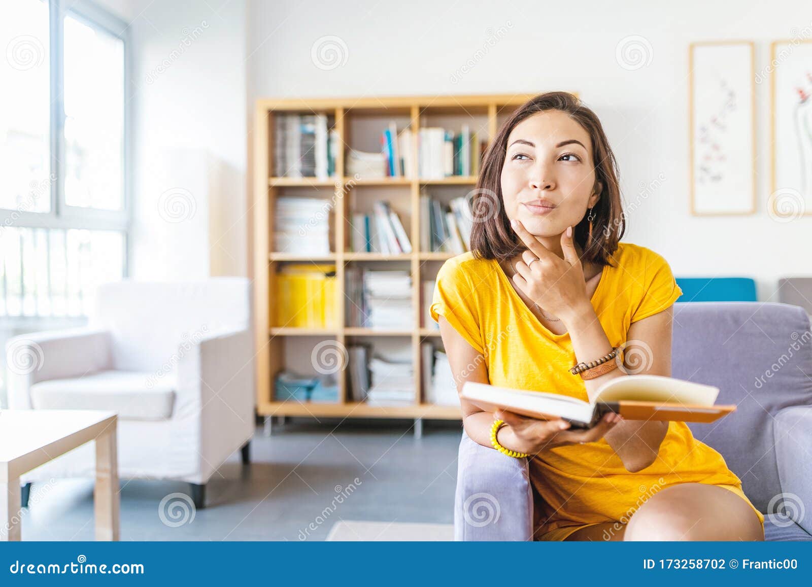 happy student woman thinking and having interesting idea while reading book in library
