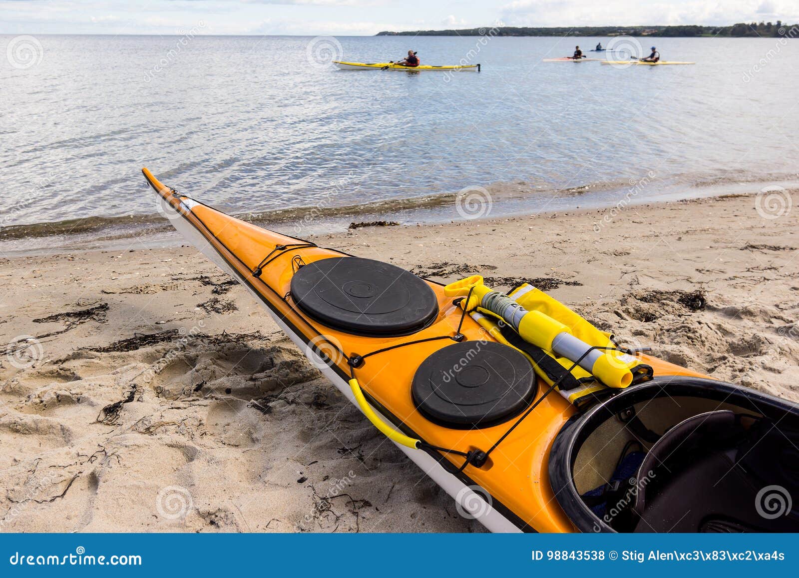Een gele overzeese kajak op het zand en vier die langs de kust kayaking. Een gele kajak op het strand en vier die langs de kust, Holl, Denemarken, 27 Augustus, 2017 kayaking