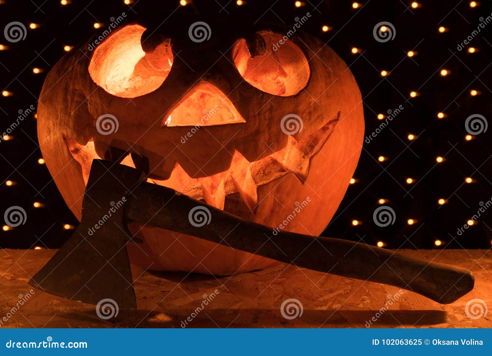 Een grappige oranje pompoen zoals een hoofd met gesneden ogen en een glimlach met het branden van kaarsen en een bijl op een zwarte achtergrond met een slinger voor de Halloween-partij