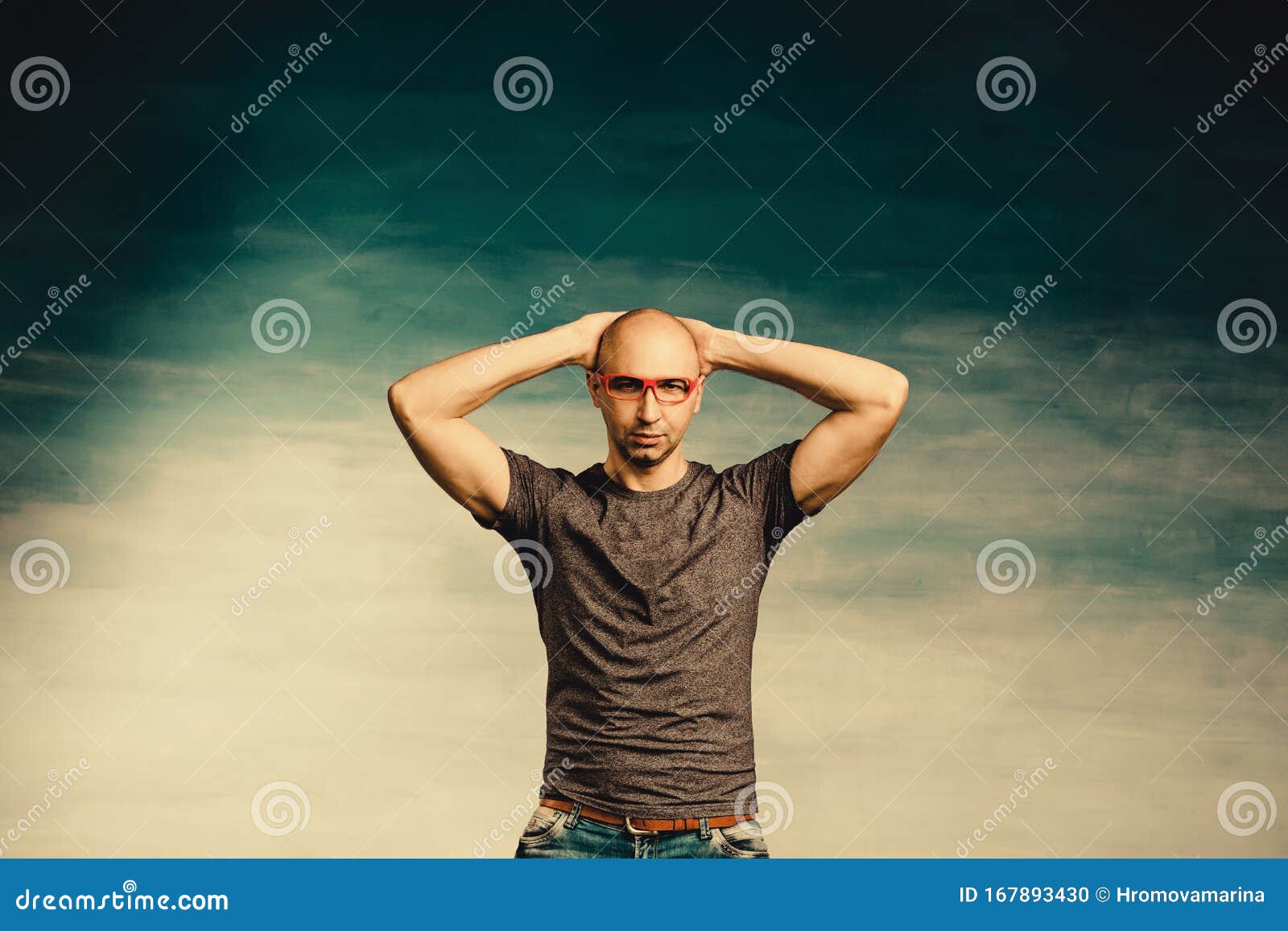 Een Interessante Kale Man In Een Rode Bril Staat Tegen Een Blauwe Muur Met Zijn Handen Achter Zijn Hoofd Stock Foto - Image Of Lichaam, Menselijk: 167893430