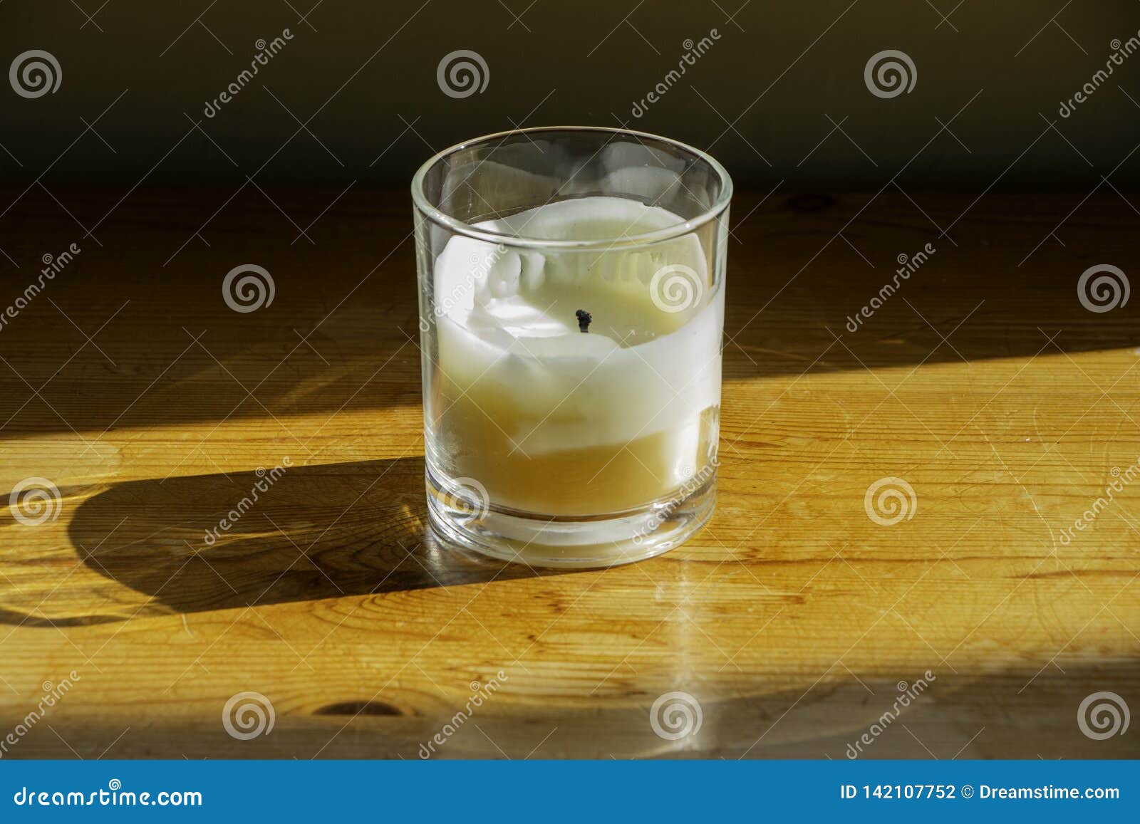 Een witte kaars in een glaskruik op een houten worktop van verder terug