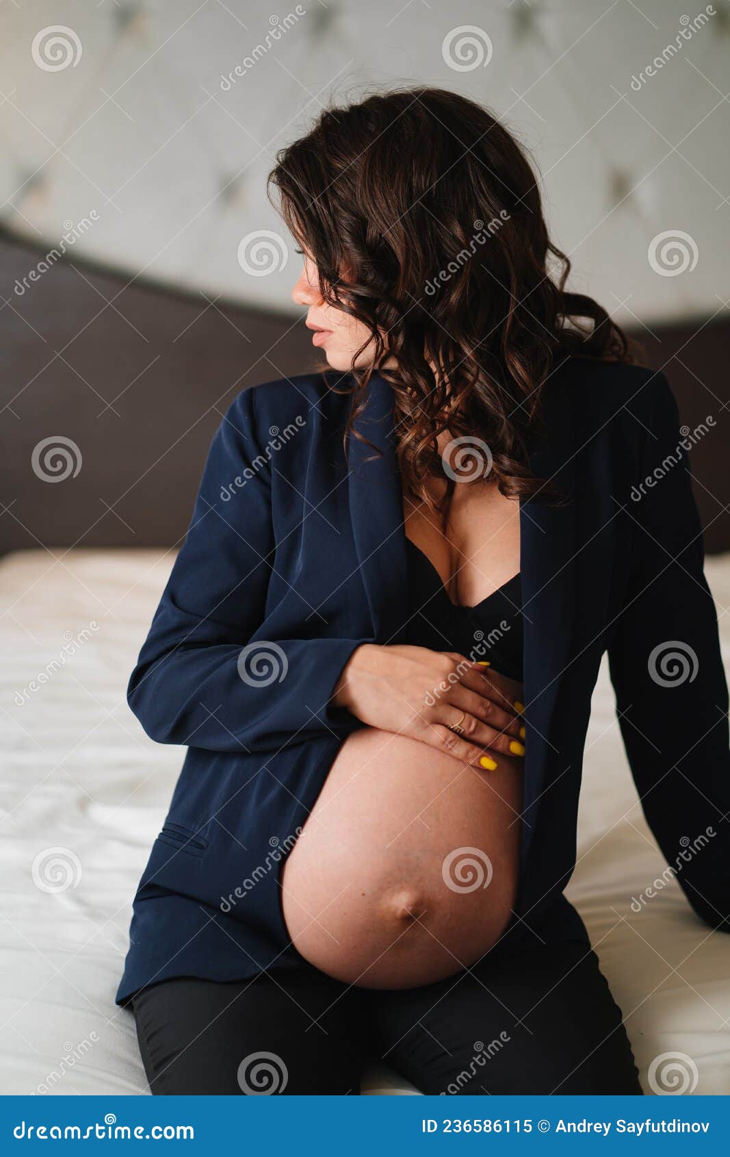 Een Zwangere Vrouw in Een Zwarte Jas Met Blote Borsten En Een Buik Op Bed Stock Afbeelding afbeelding foto