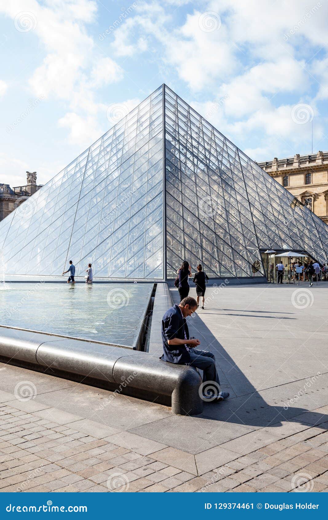 Ein Mann, der nahe bei der Glaspyramide des Louvre sitzt. Ein Mann sitzen nahe bei der Glaspyramide des Louvre am frühen Morgen im Sommer