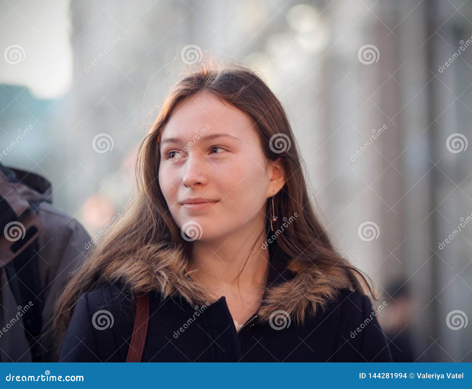 Ein Mädchen mit einem Lächeln, das einen Passanten betrachtet. Ein Mädchen mit dem langen braunen Haar, gehend hinunter die Straße von einer Großstadt, wenn ein Lächeln betrachtet, einen Passanten