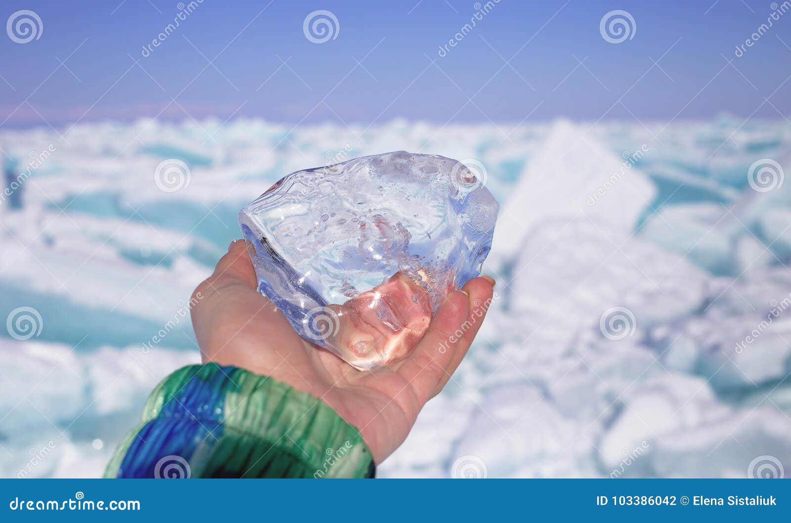 Ein Stück transparentes Kristalleis in der Hand gegen gefrorenen See am sonnigen Tag