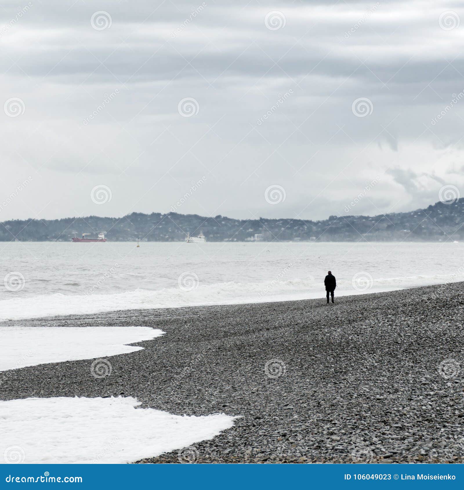 Einsamer Mann in der schwarzen Kleidung steht auf der Küste an einem bewölkten Tag