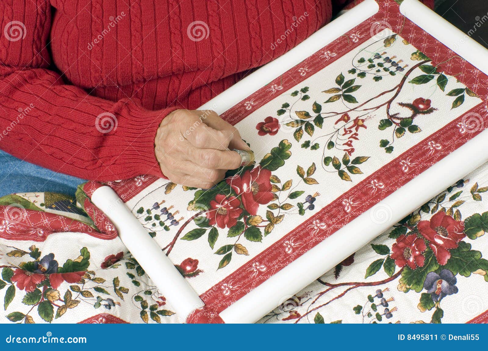 El acolchar de la mano de la mujer. Una mano de la mujer que acolcha un edredón del algodón usando un marco plástico.