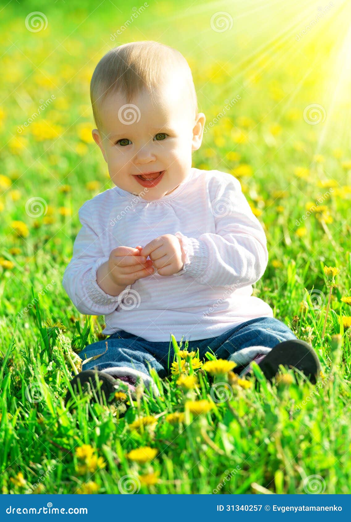 El bebé en un prado verde con amarillo florece los dientes de león en el th. El pequeño bebé feliz hermoso que se sienta en un prado verde con amarillo florece los dientes de león en la naturaleza en el parque