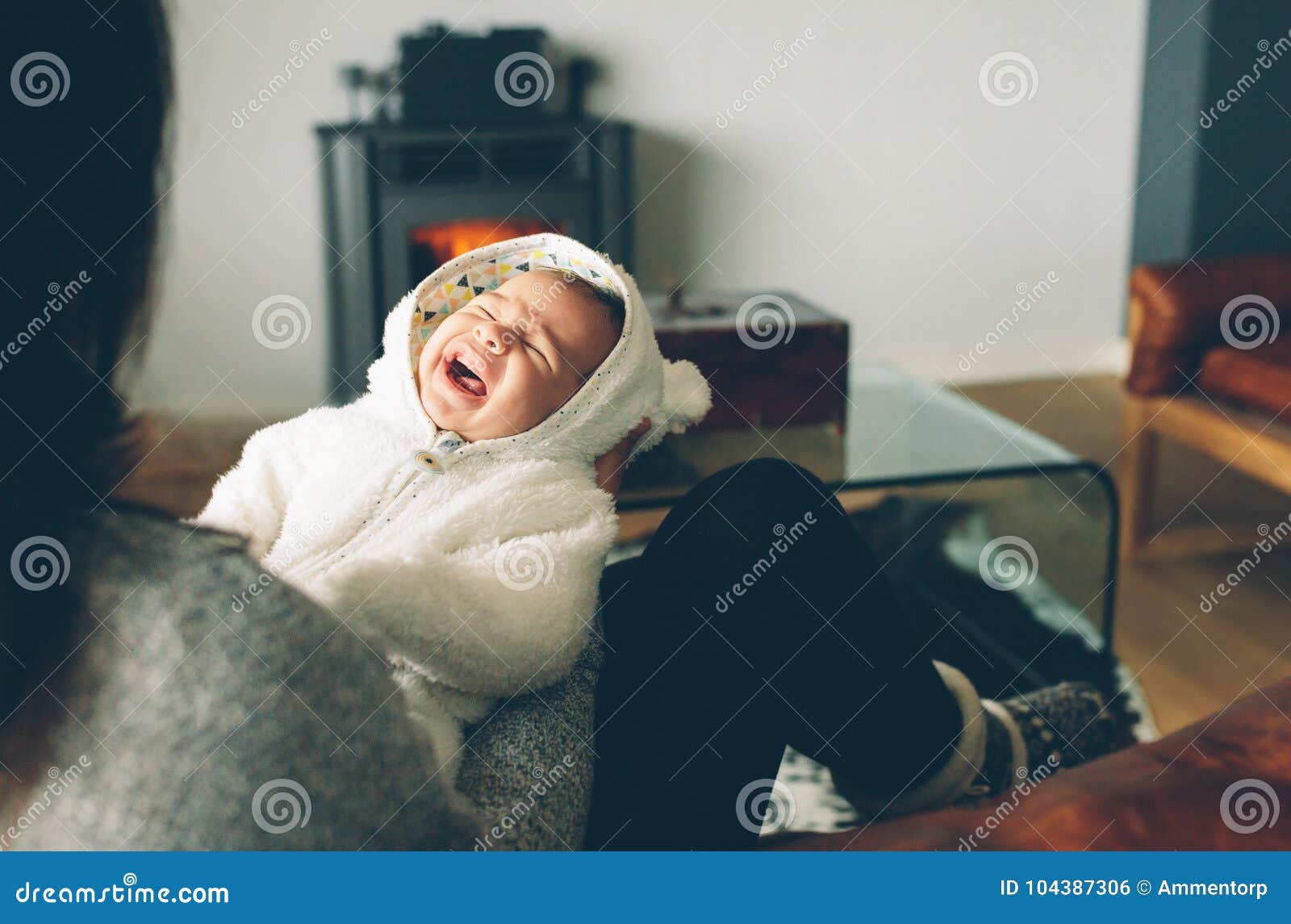 El bebé recién nacido que llora en su ` s de la madre arma Mujer que se sienta en el sofá con su bebé gritador en casa