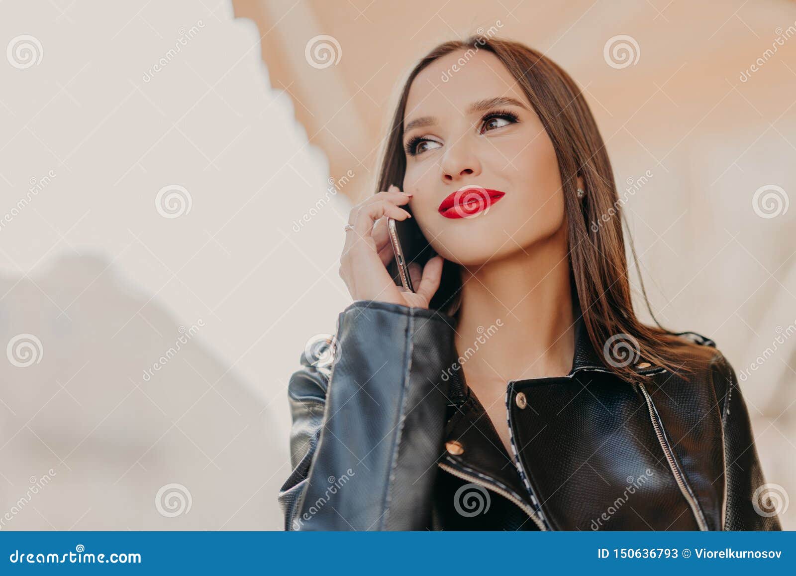 El Headshot De La Mujer Soñadora De Mirada Agradable Enfocada a Un Lado,  Tiene Conversación Telefónica, Lleva La Capa De Cuero, N Imagen de archivo  - Imagen de dispositivo, hablar: 150636793