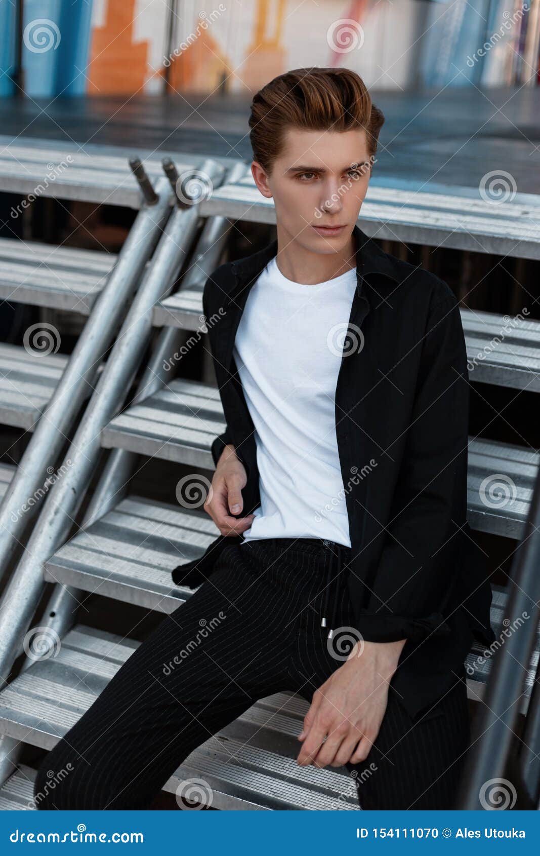 El Hombre Joven Atractivo En Una Camisa Elegante En Una Camiseta En Pantalones Rayados De Moda Se Esta Sentando En Una Escalera D Foto De Archivo Imagen De Sentando Joven 154111070