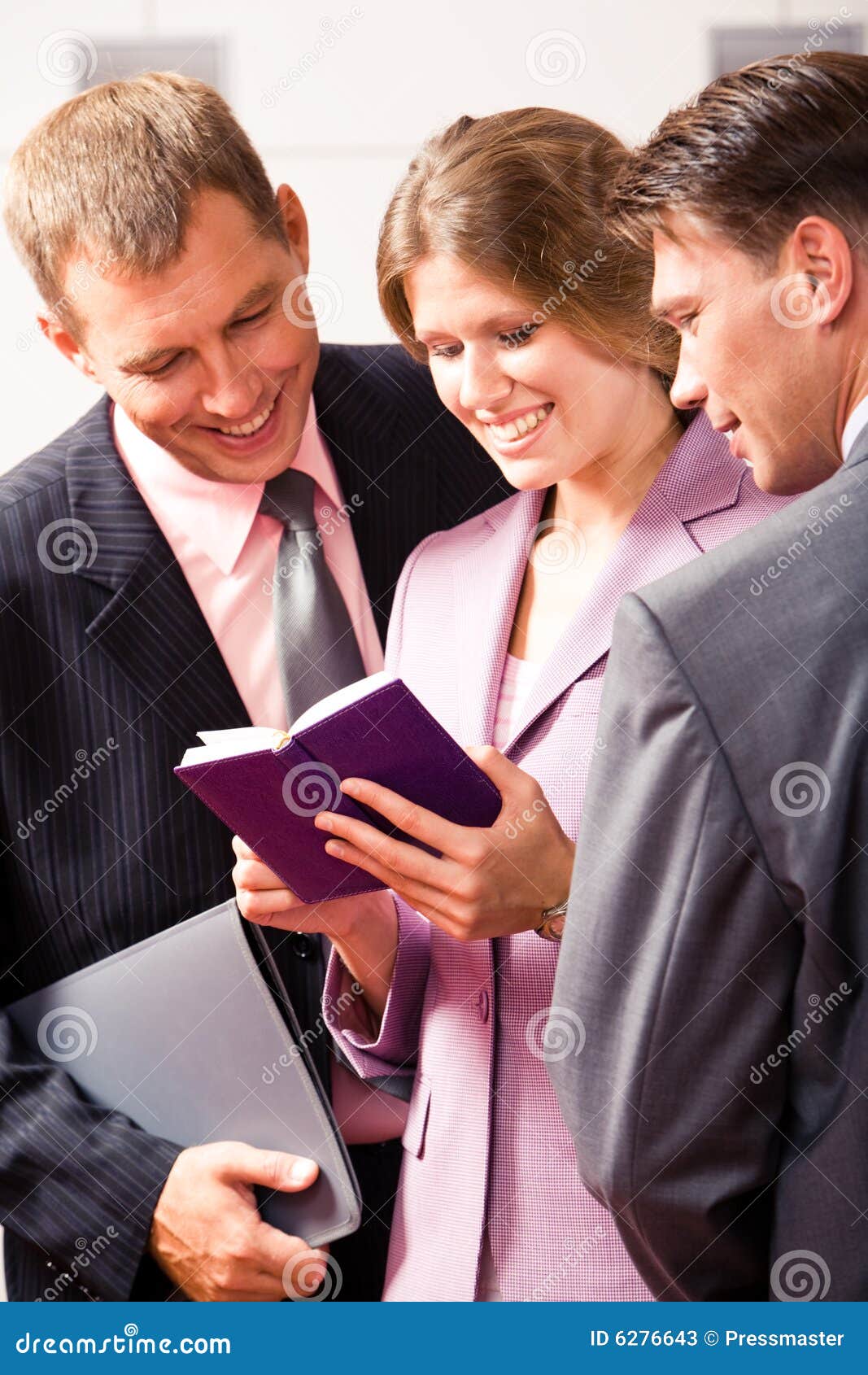 El obrar recíprocamente. Tres socios comerciales acertados que miran en el cuaderno en manos de los woman?s con sonrisas