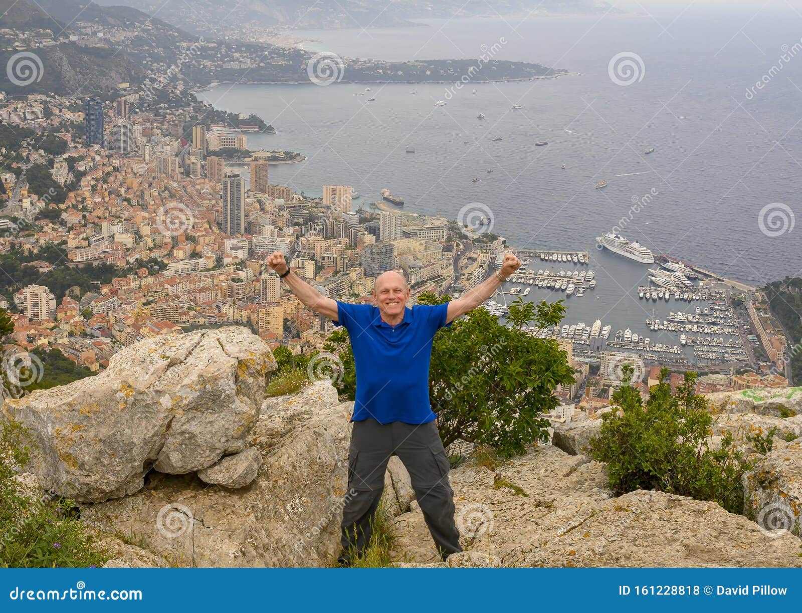 elderly caucasian male amerasian tourist posing on tete de chien, with a vew of monaco in the background.