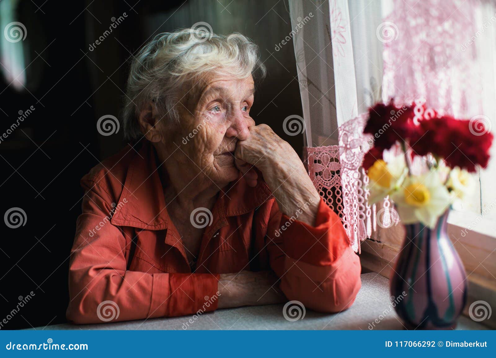 elderly lone woman looks sadly out the window.
