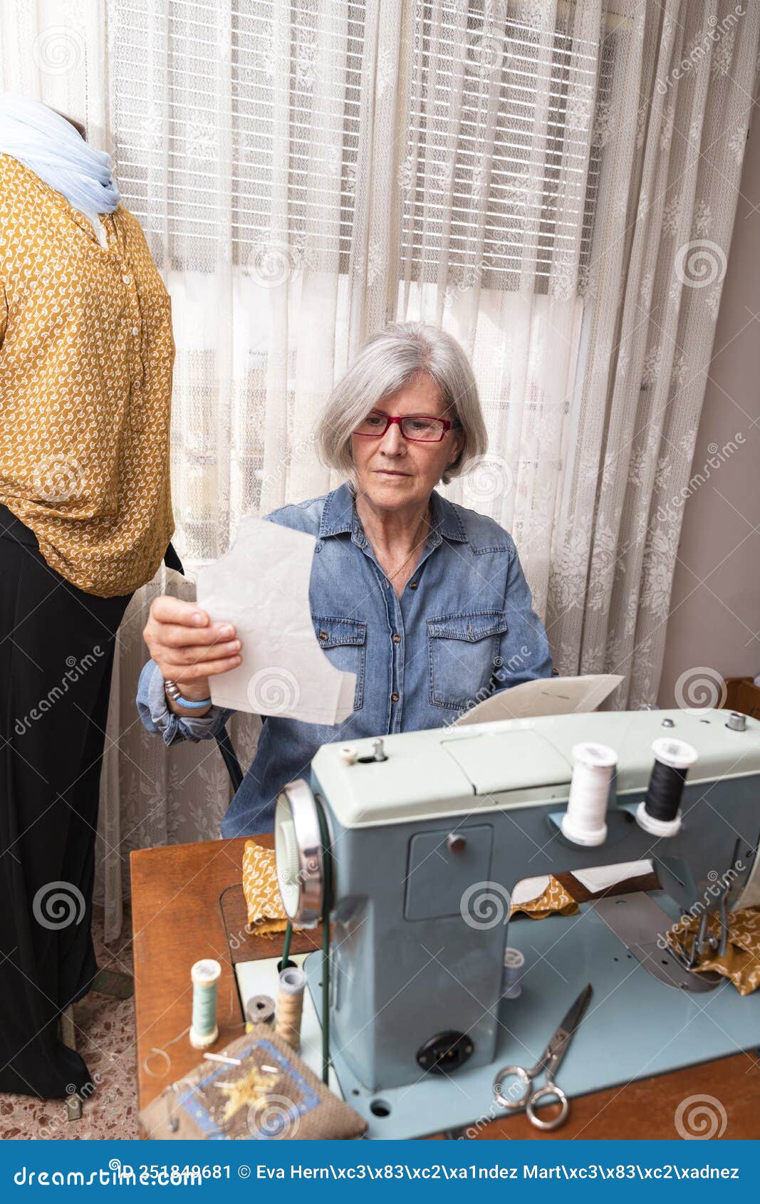 Elderly Woman Checking a Sewing Pattern Next To a Sewing Machine Stock