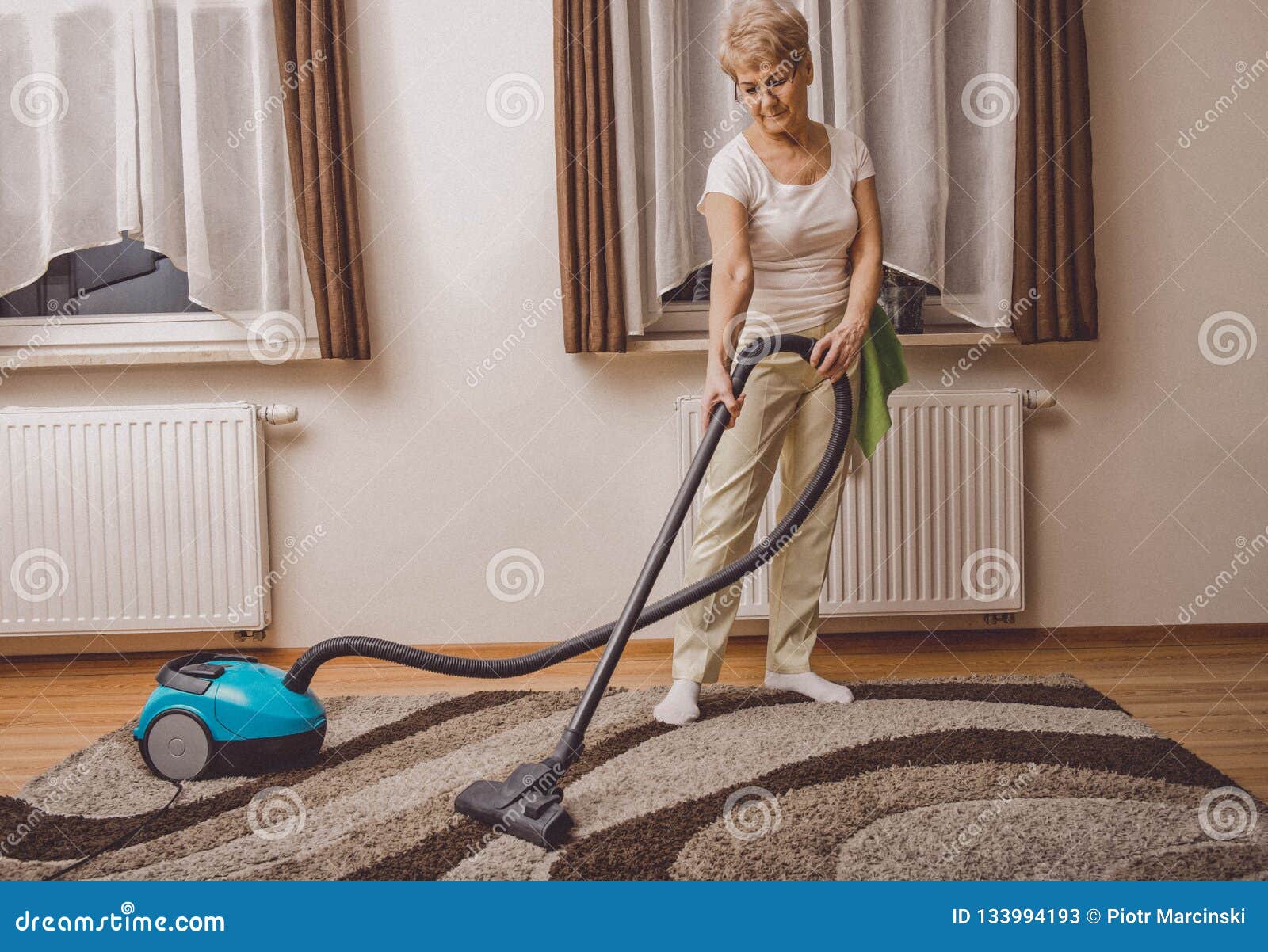elderly woman doing woman chores at home. vacumming the carpet