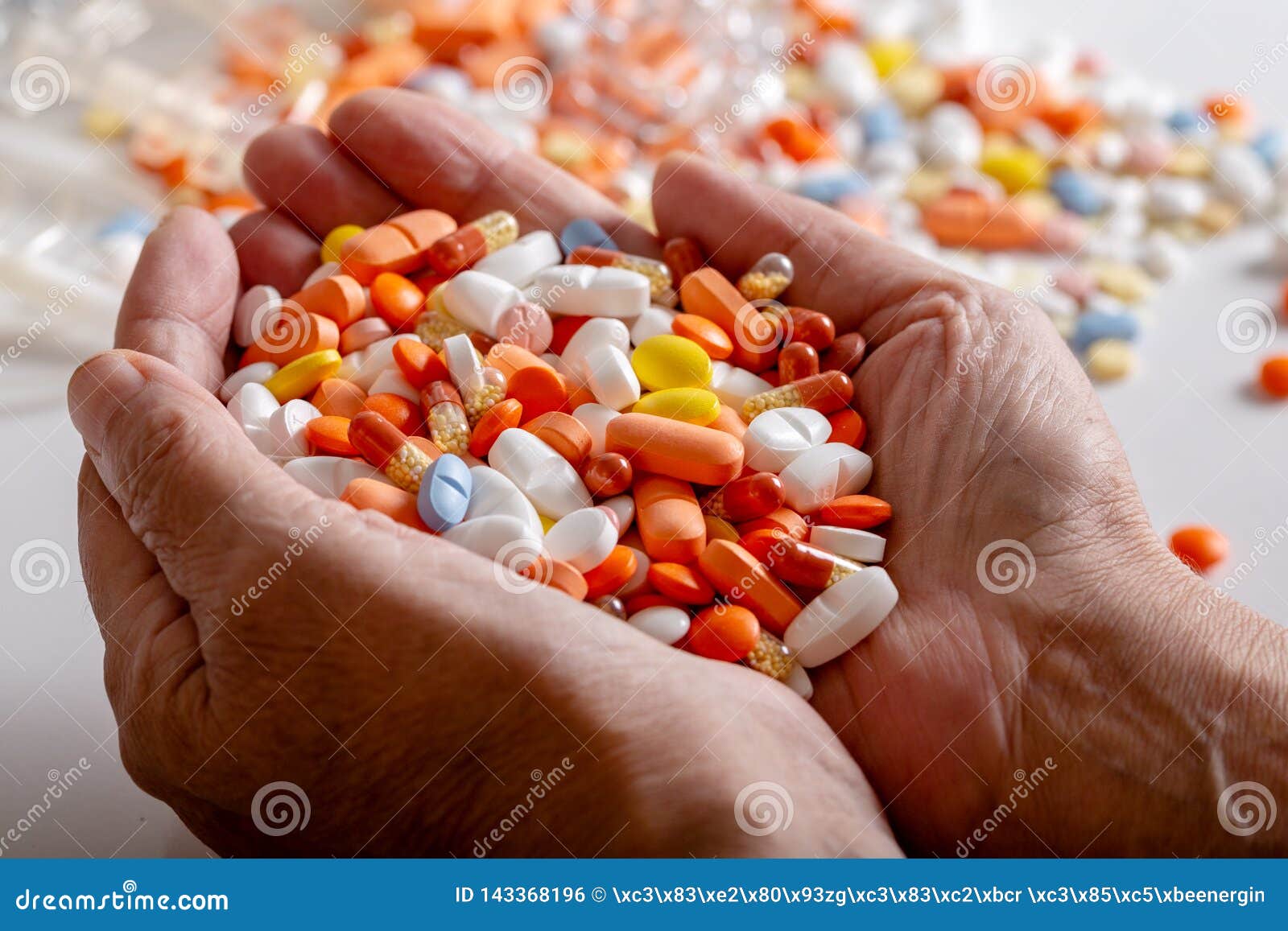 an elderly woman holds a lots of colored pills in hands on a white background.