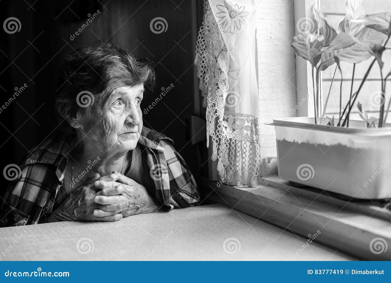 Elderly woman looks wistfully out the window. Black-and-white photo.
