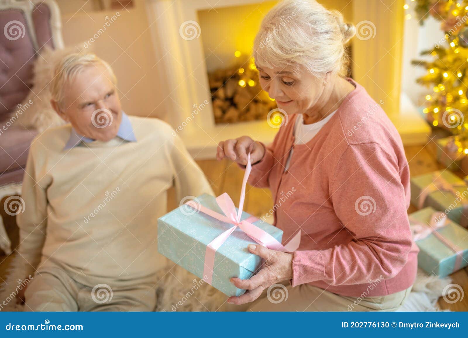 elderly woman opening christmas gift from her husband and looking anticipated