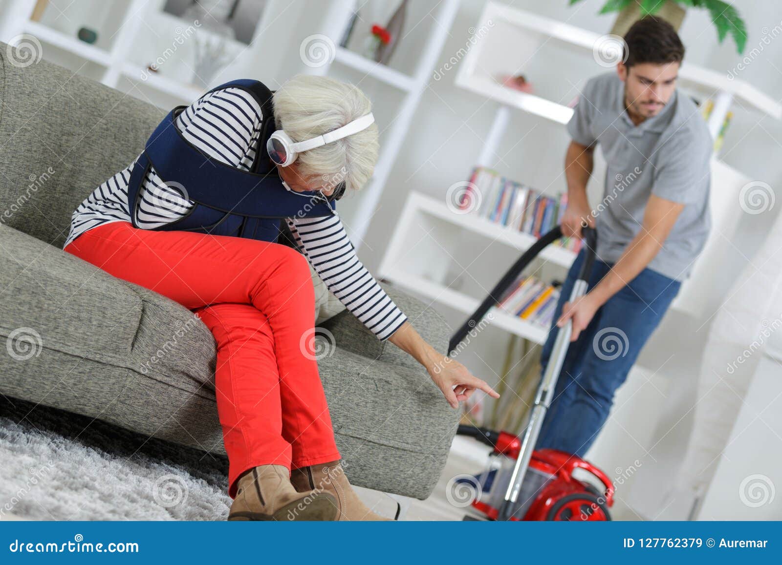 Elderly Woman on Sofa while Housekeeper Hoovers Stock Image Image of