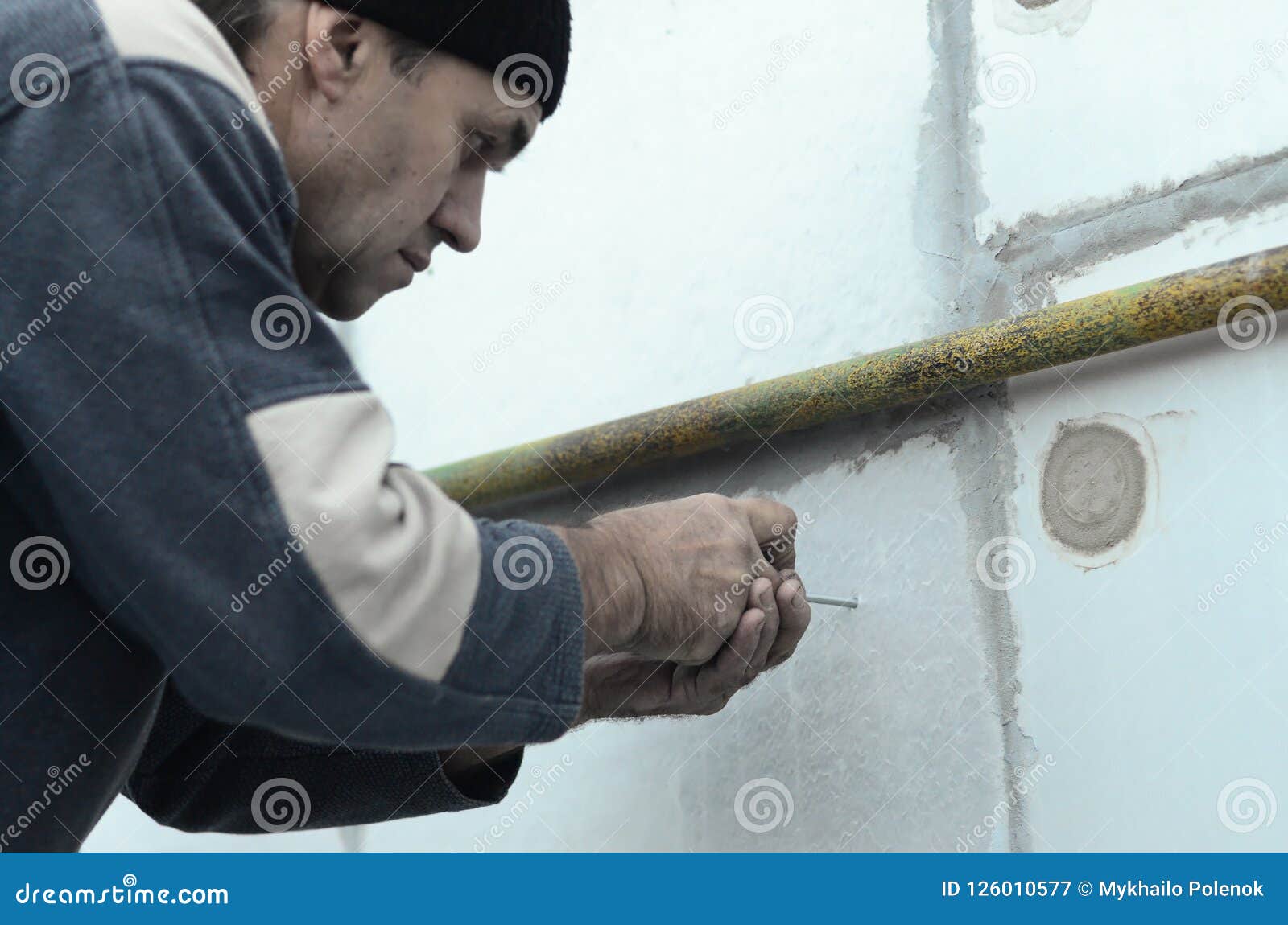 An Elderly Worker Creates Holes in the Expanded Polystyrene Wall for