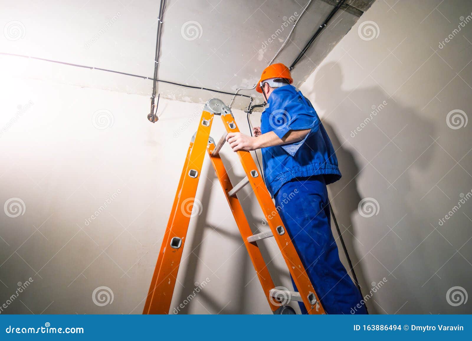 Electrician in Hard Hat and Uniform Standing on Step Ladder Stock Photo
