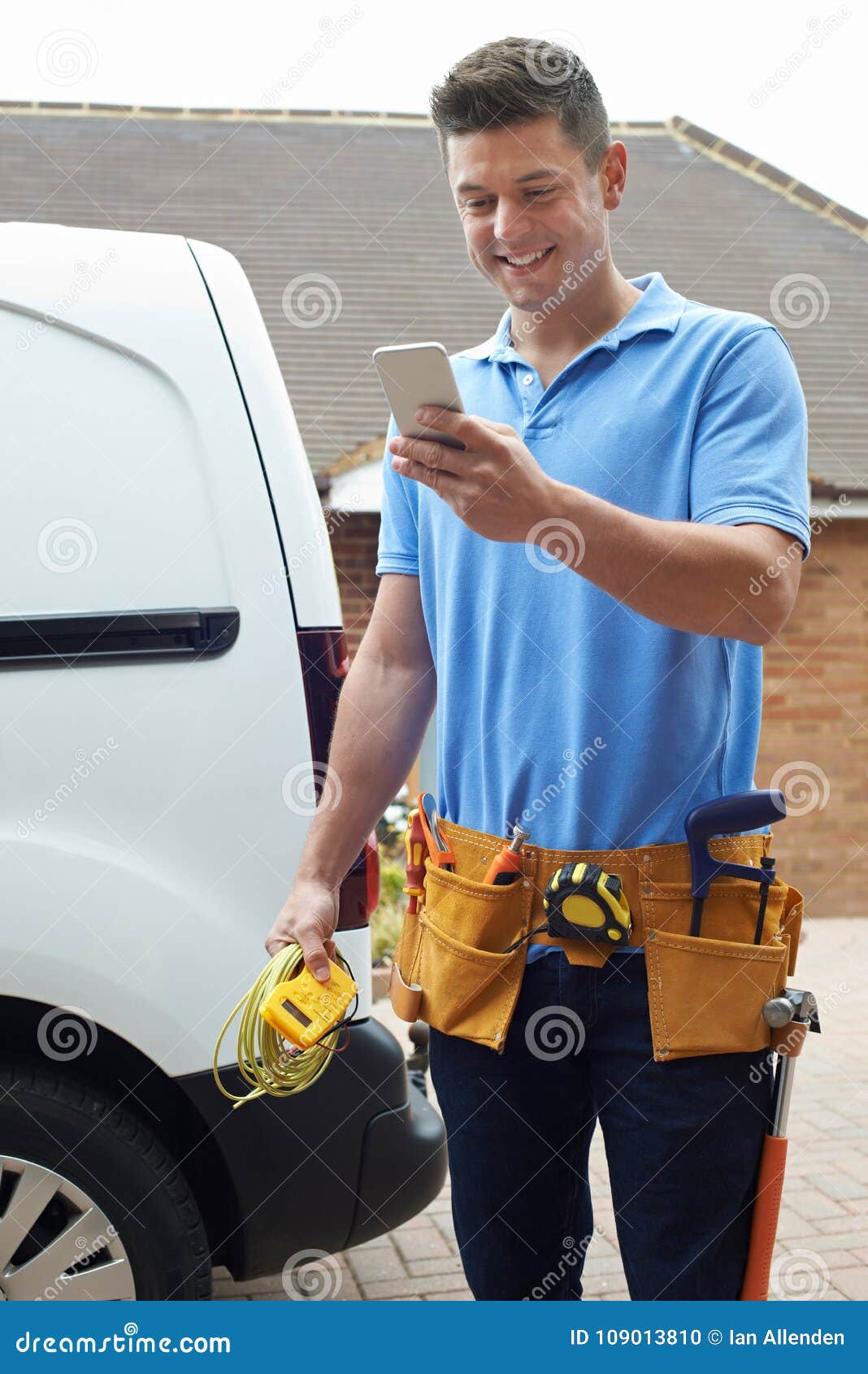 electrician with van texting on mobile phone outside house