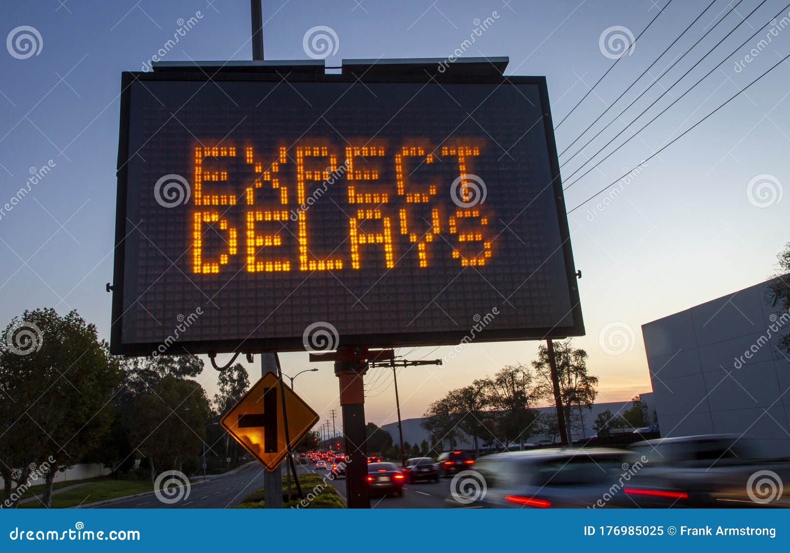 electronic traffic sign stating expect delays with blurred traffic at sunset