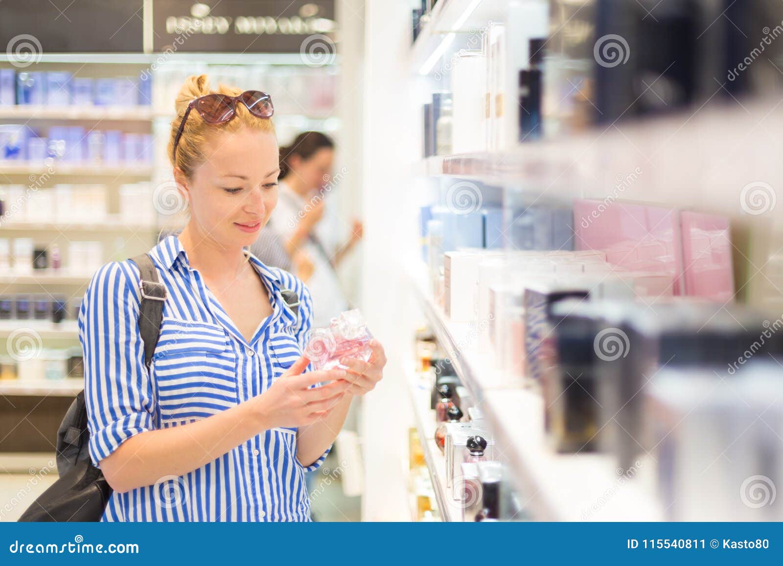 elegant blond young woman choosing perfume in retail store.