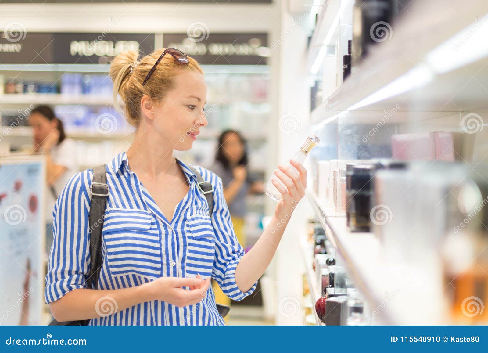 elegant blond young woman choosing perfume in retail store.
