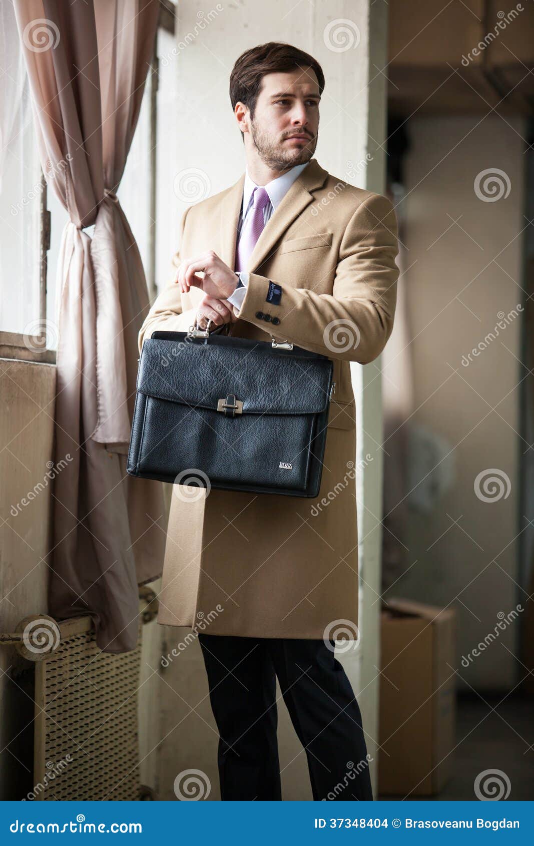 Elegant man looking to the left side. Classic and elegant businessman wearing beige coat labeled, white chemise and pink tie, holding a black briefcase and looking to his left side