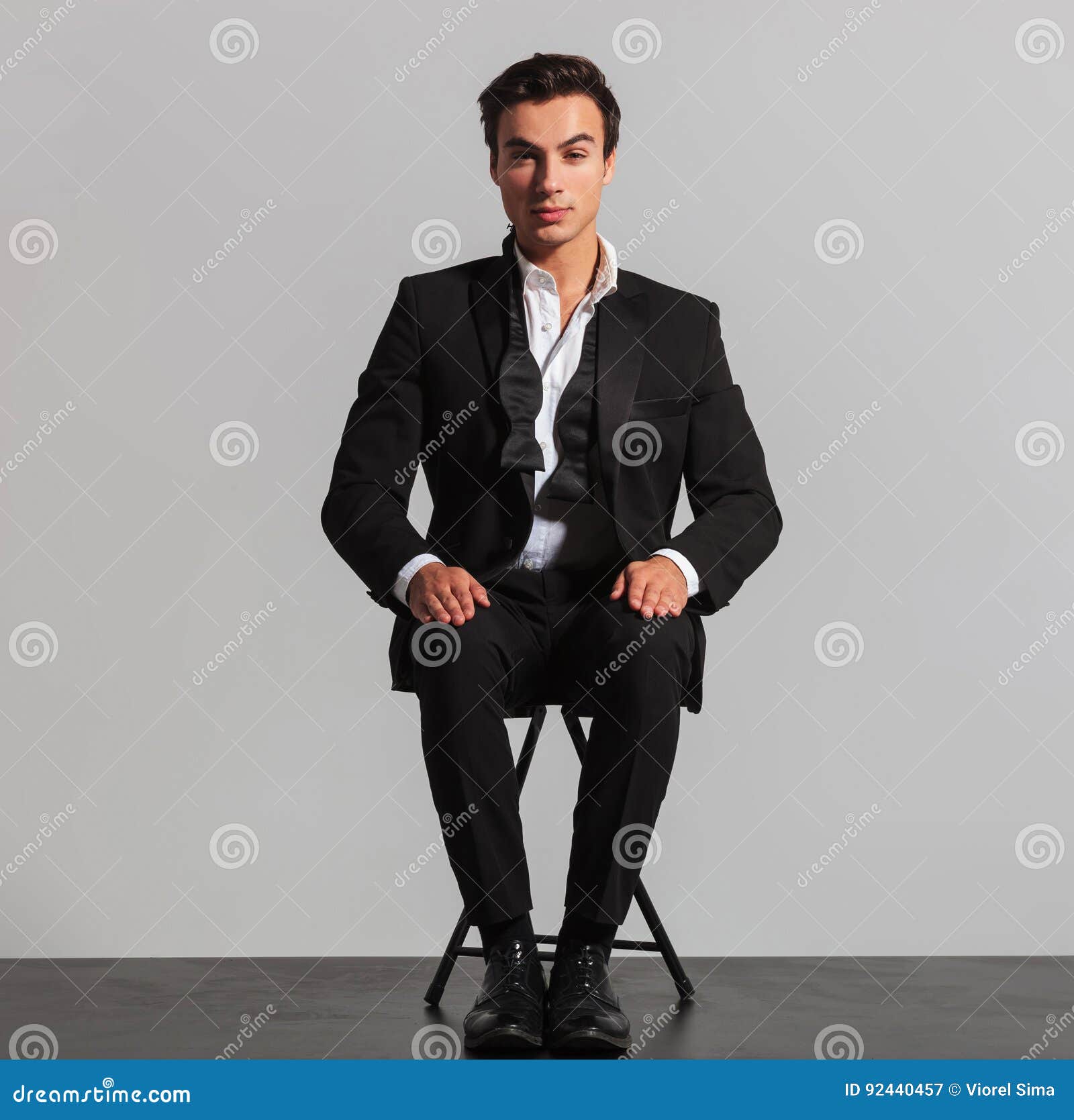 elegant man in suit and undone bowtie sitting on chair