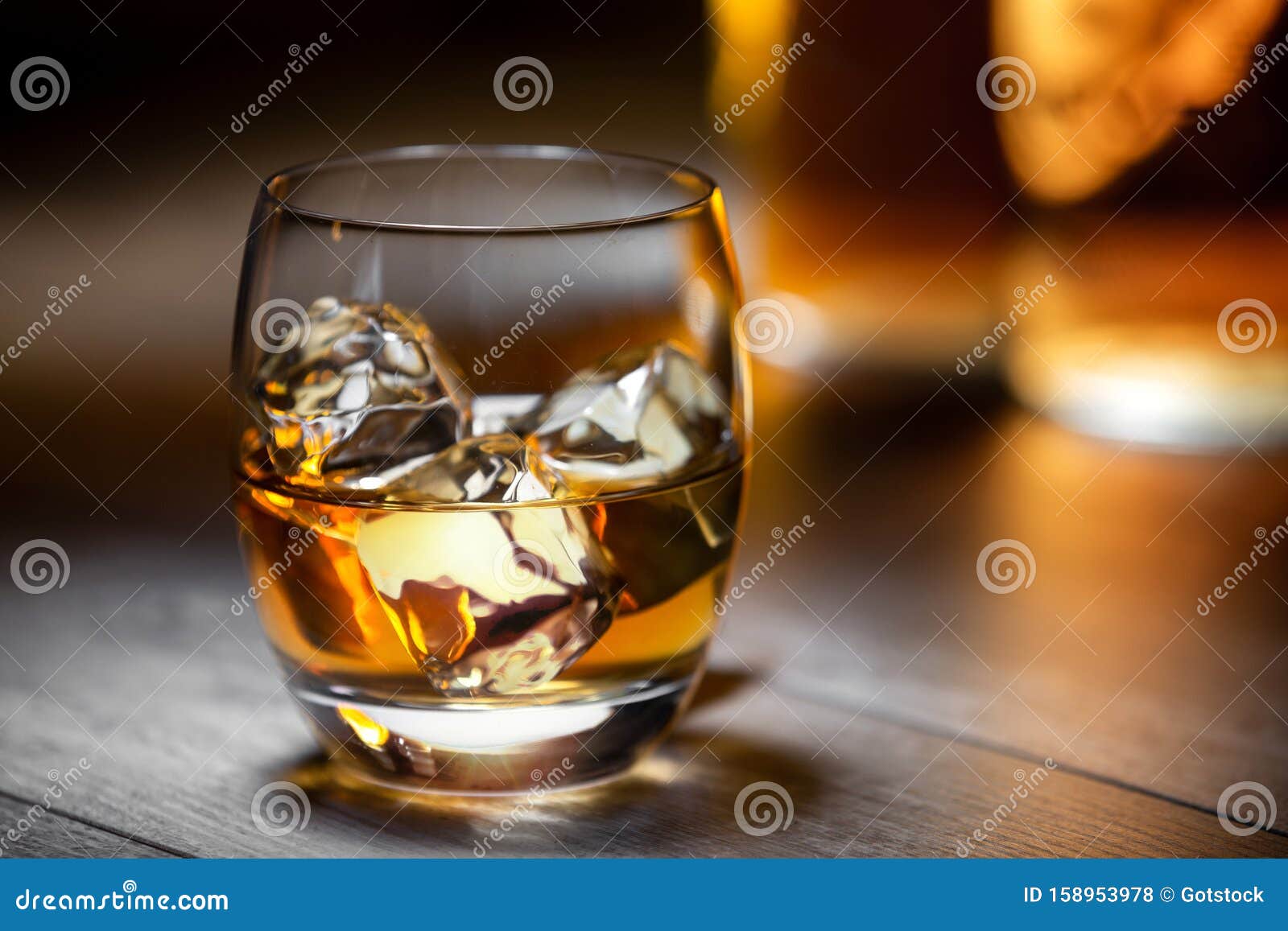 elegant and refreshing glass of scotch bourbon whisky on ice with glowing illuminated golden bottles in background, copy space