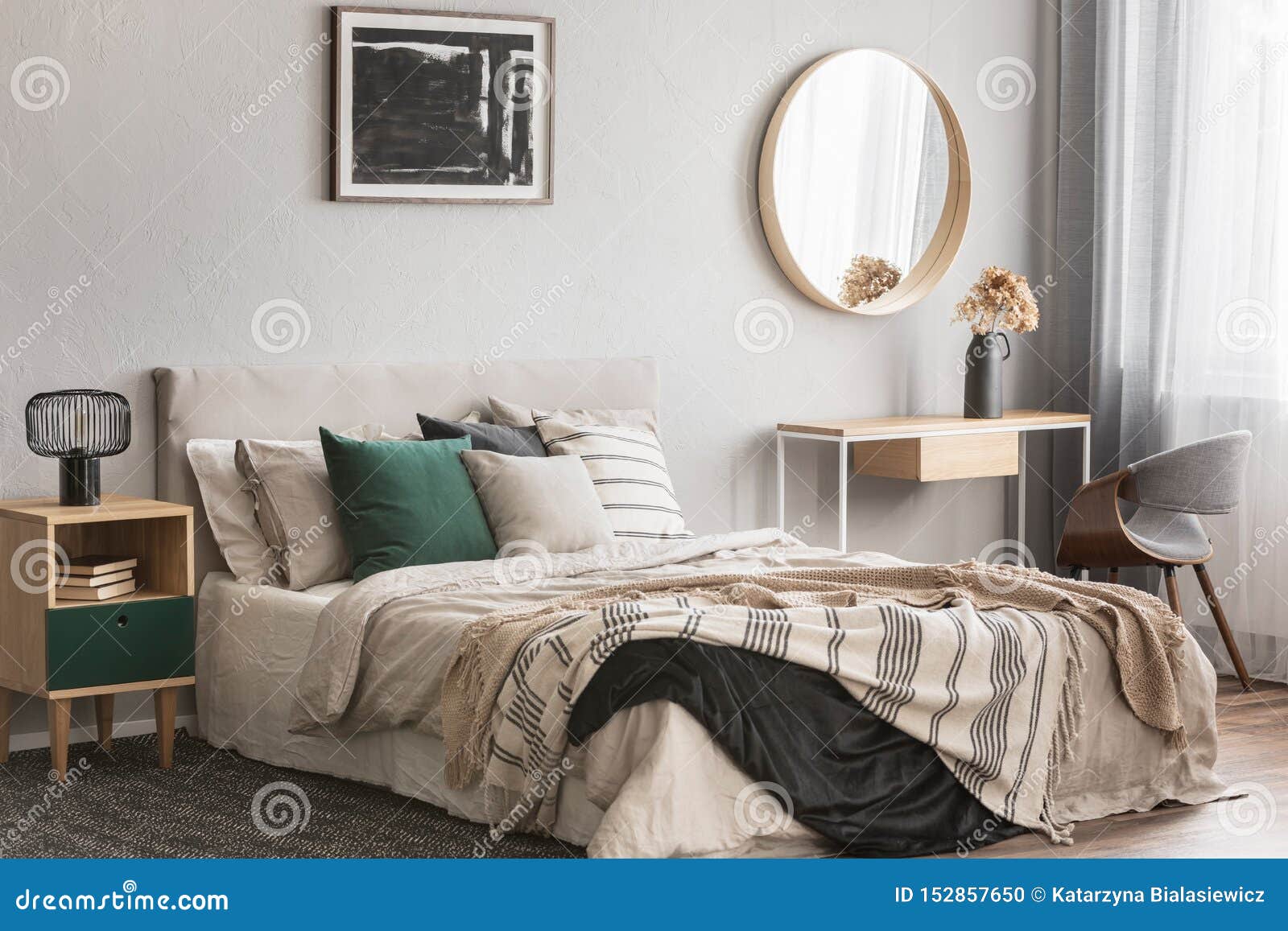 elegant round mirror in wooden frame above fancy console table with flowers in vase in trendy bedroom interior with beige vase