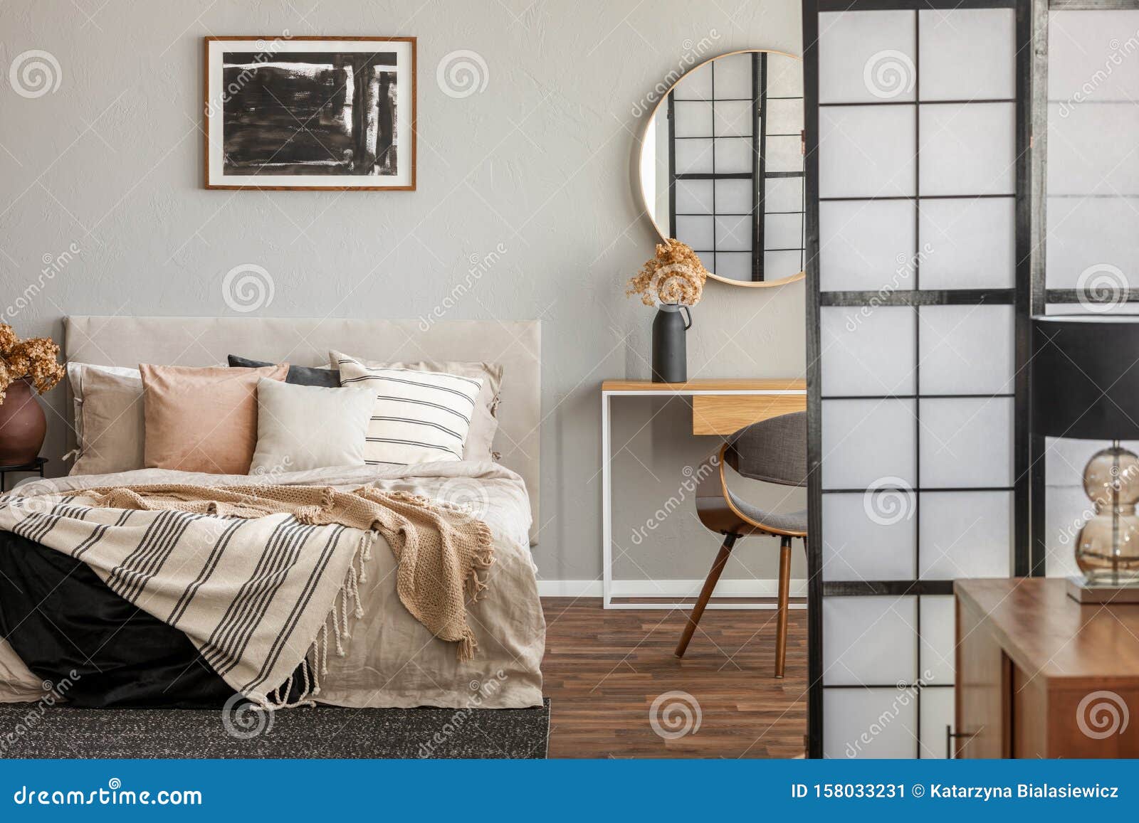 elegant mirror in wooden frame above fancy console table with flowers in vase in trendy bedroom interior with beige vase