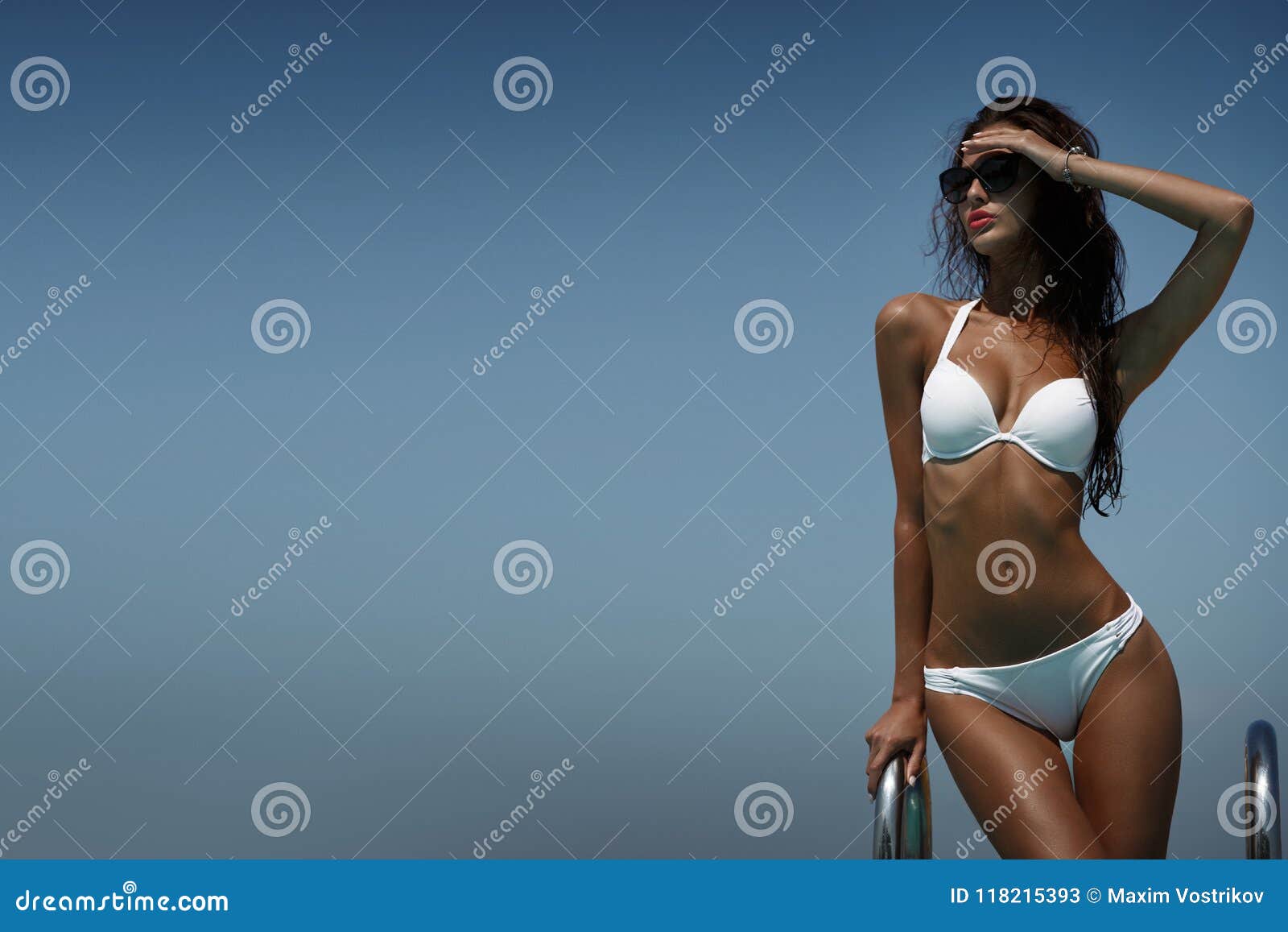 Foto de Elegant sexy woman in luxury bikini on the sun-tanned slim and shapely  body is posing in the studio on a white background - Image. Bikini model.  Bikini sexy concept. Summer