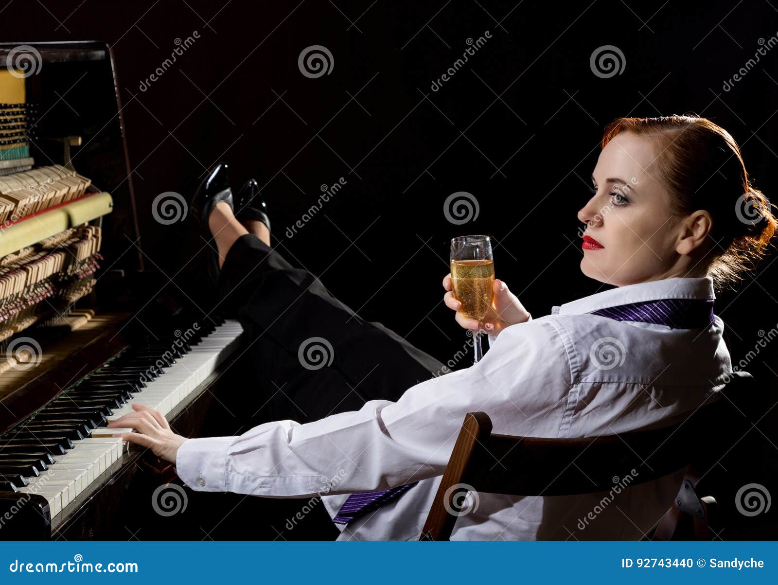 elegant woman in a white shirt and tie sitting next to the piano and drinks champagne