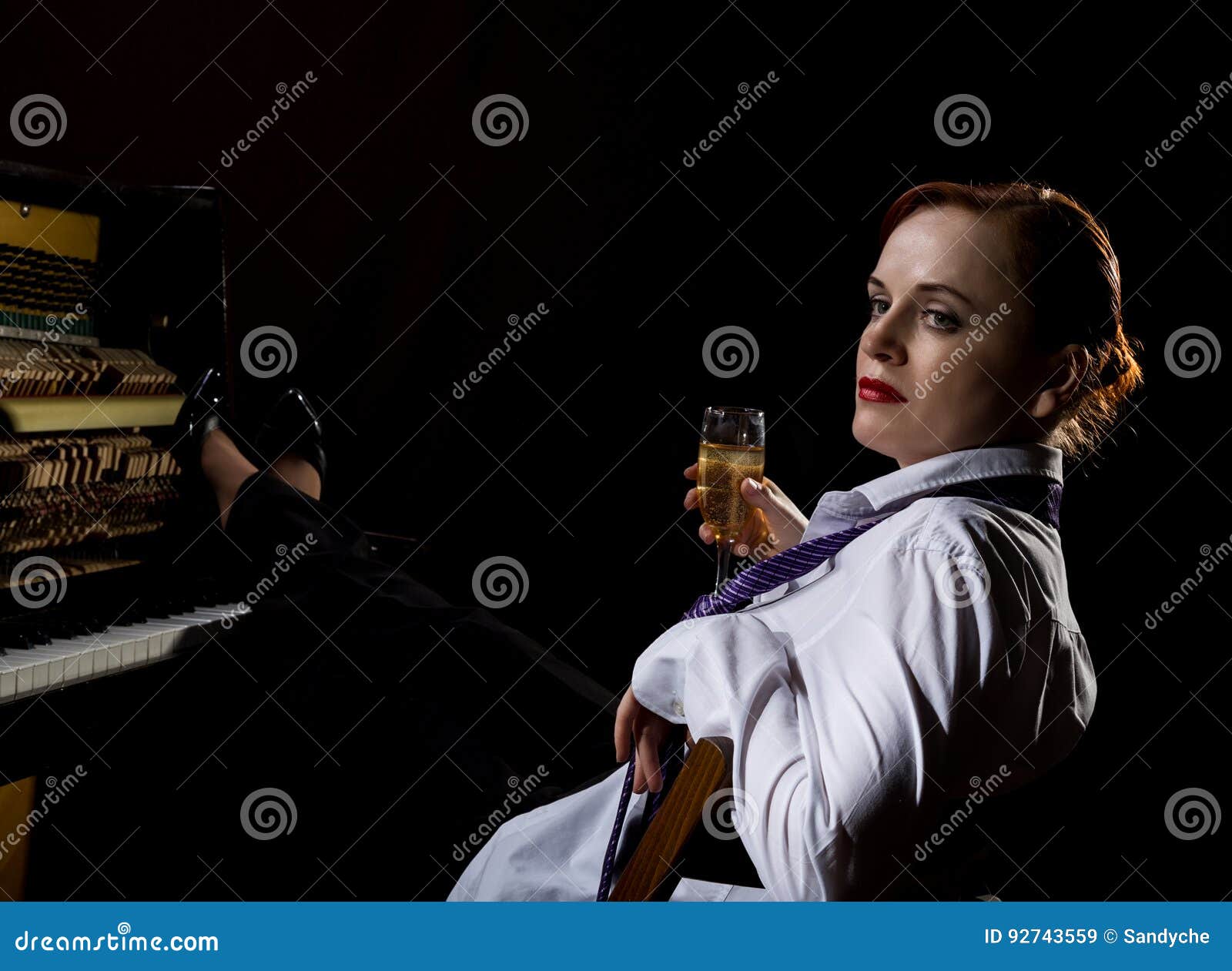 elegant woman in a white shirt and tie sitting next to the piano and drinks champagne